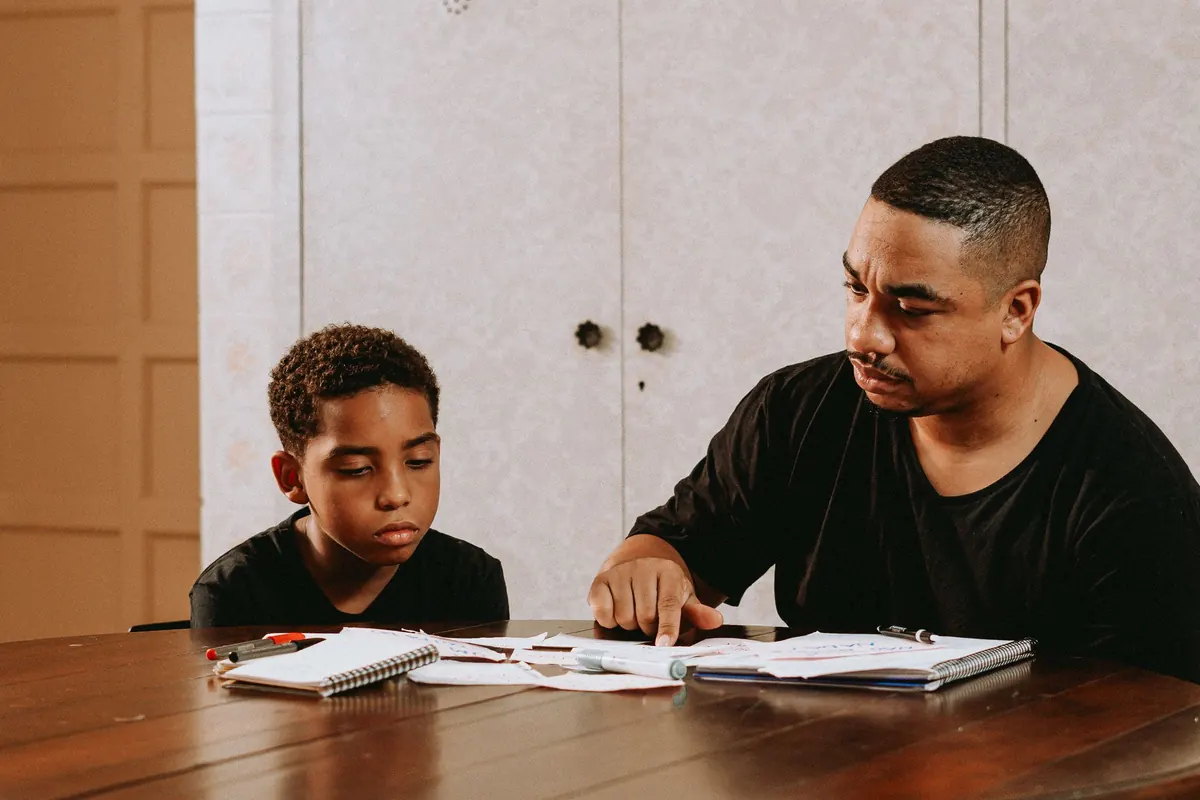 A father helping his son with homework at a wooden dining table