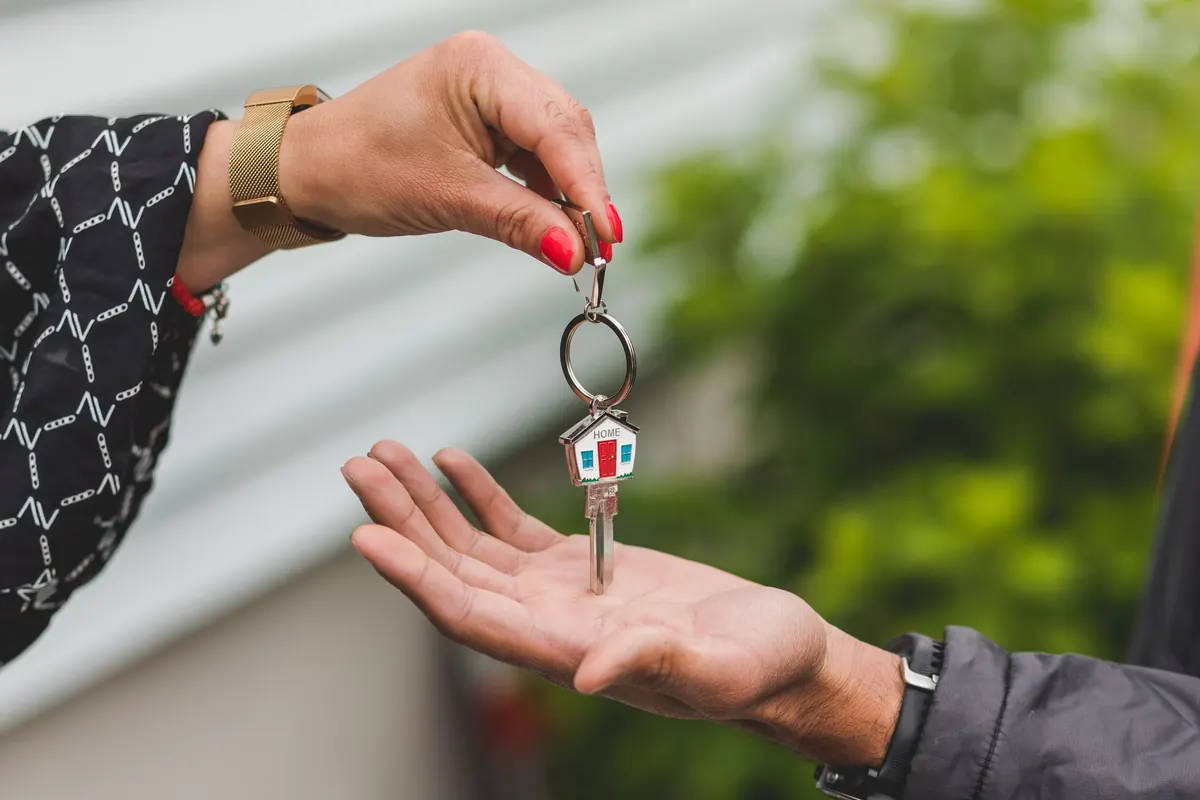 A hand passing a house key on a house-shaped keyring into another person's open palm