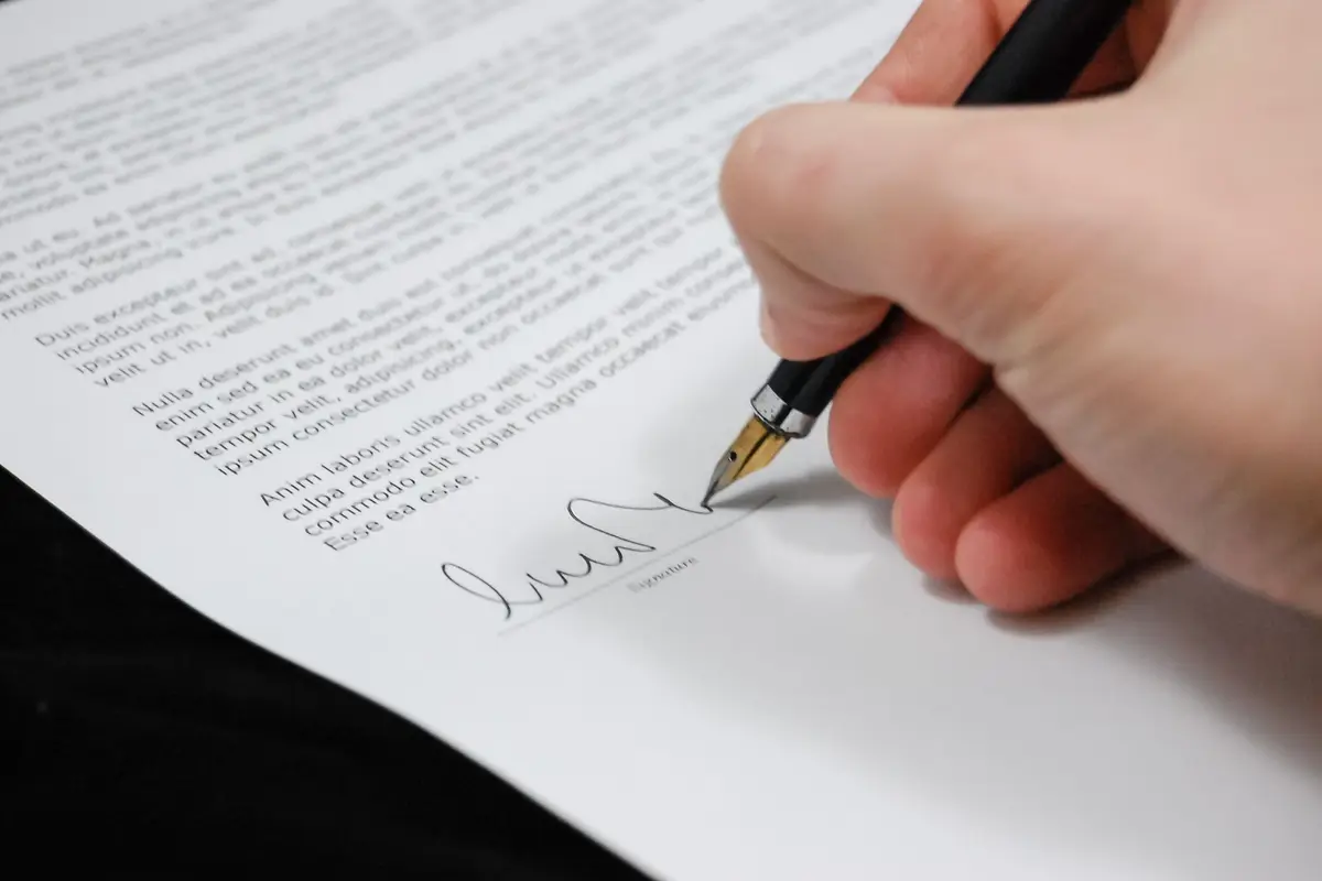 A hand signing a printed agreement with a fountain pen
